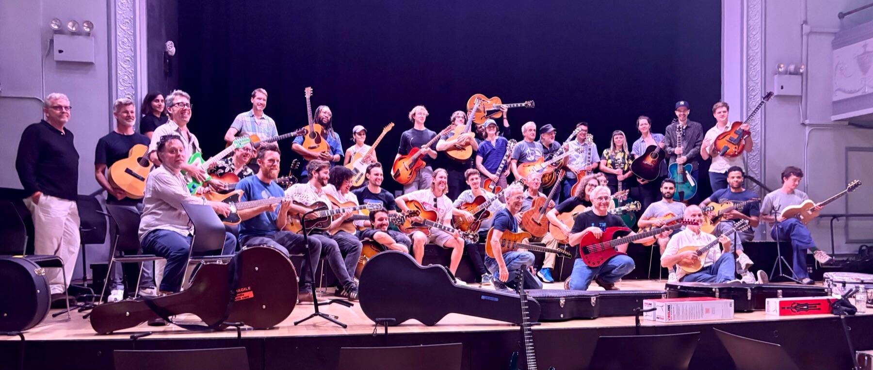 A large group of Brooklyn Guitar Feast II attendees holding guitars on stage.